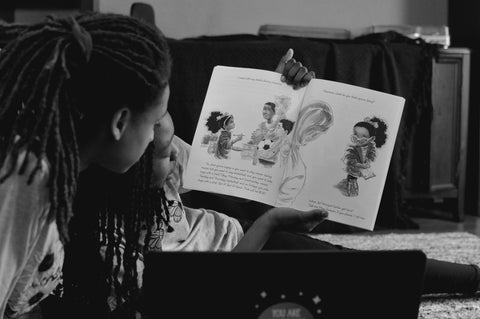 Black child with locs reading a book with Black adult with locs