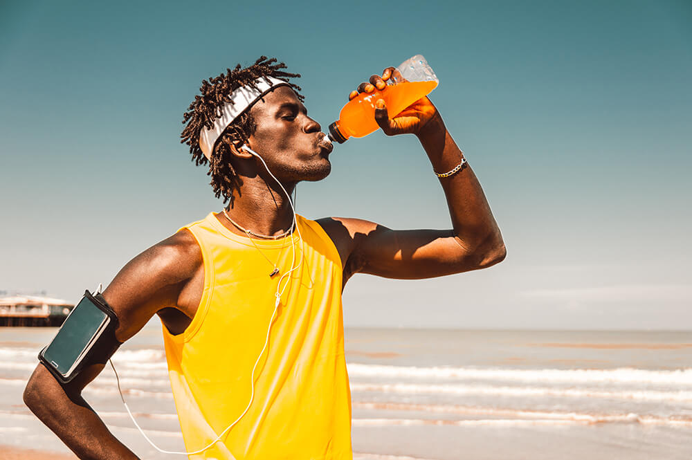 Man drinking an energy drink at the beach after a workout