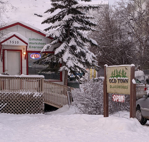The outside of Old Town Glassworks in the winter. The snow covered red and white exterior of the showroom and the wooden sign can be seen.