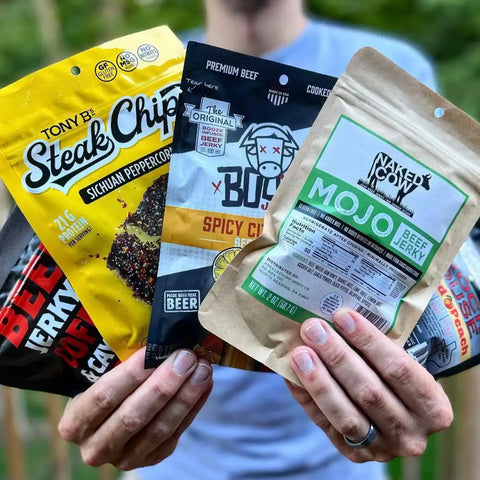 Beef jerky variety from the largest selection of craft beef jerky on the web, showing 5 delicious flavors from different brands being held up by two hands.