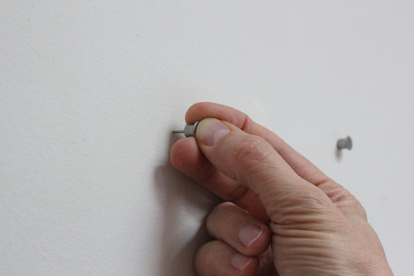 A thumb inserts the Collagewall push pin into the wall