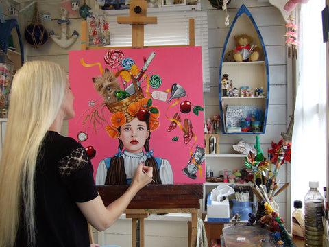 Artist Marie Louise Wrightson busy painting in her studio surrounded by seaside novelties and her collection of Alice in Wonderland books and memorabilia. Marie's paintings and prints are available from The Acorn Gallery in Pocklington, online or in store, with delivery too if required.