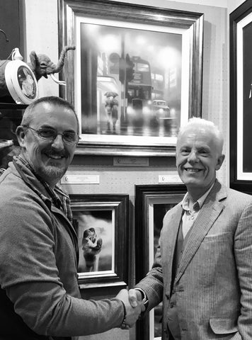 Artist Tim Shorten shaking hands with gallery owner John Wass in front of a display of original paintings and limited edition prints. All artwork available from The Acorn Gallery, Pocklington near York. 