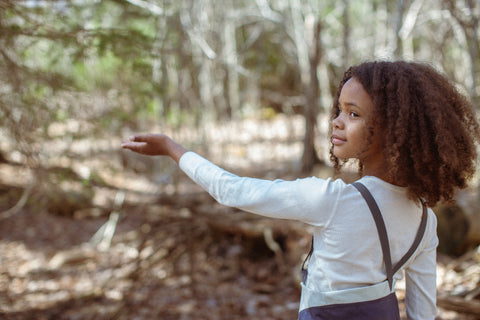 Child extending their arm in a wooded landscape.