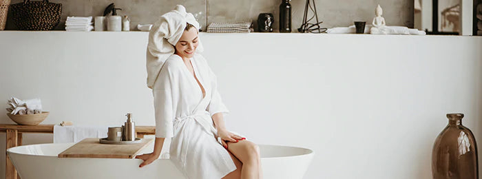A happy woman in bathrobe is sitting on the edge of bathtub
