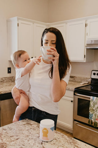 new mom drinking majka lactation booster while baby reaches for it