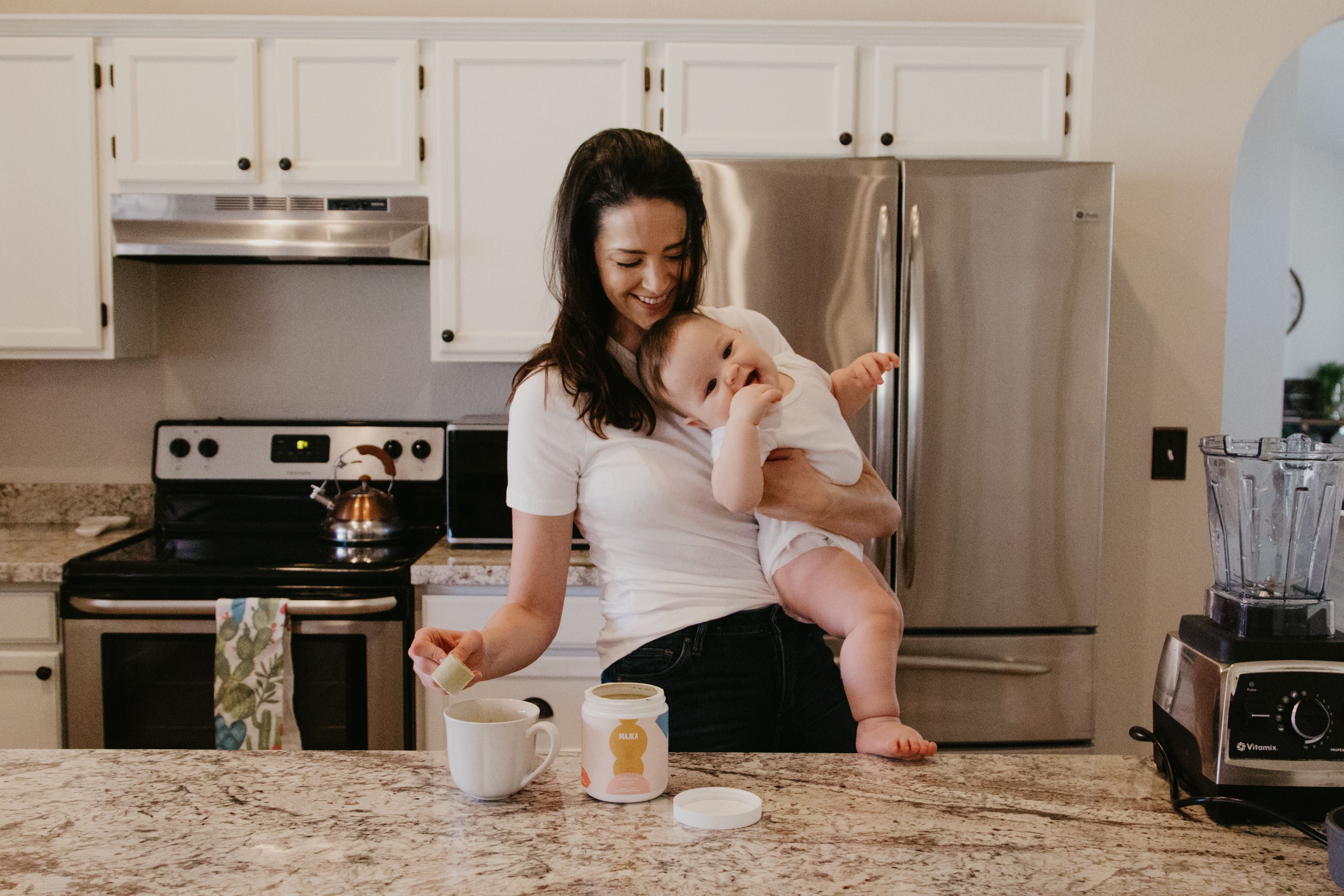 mom holding baby in kitchen making majka booster latte with shatavari