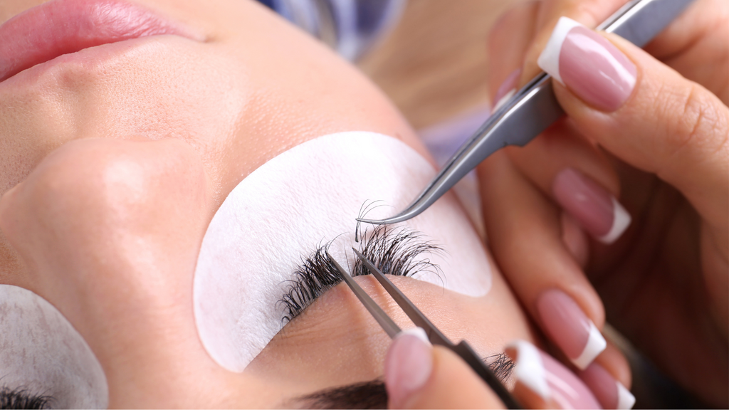 Woman lying down with a lash tech touching up her eyelash extensions.
