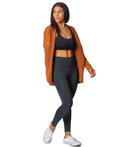Woman in black leggings, sports bra, and brown cardigan