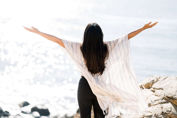 woman looking out over a sparkling ocean with outstretched arms