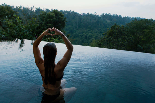 Woman in an infinity pool looking out over a lush forest