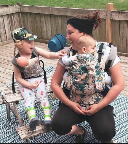 woman wearing a baby in a tula carrier while daughter wears in a mini toy carrier