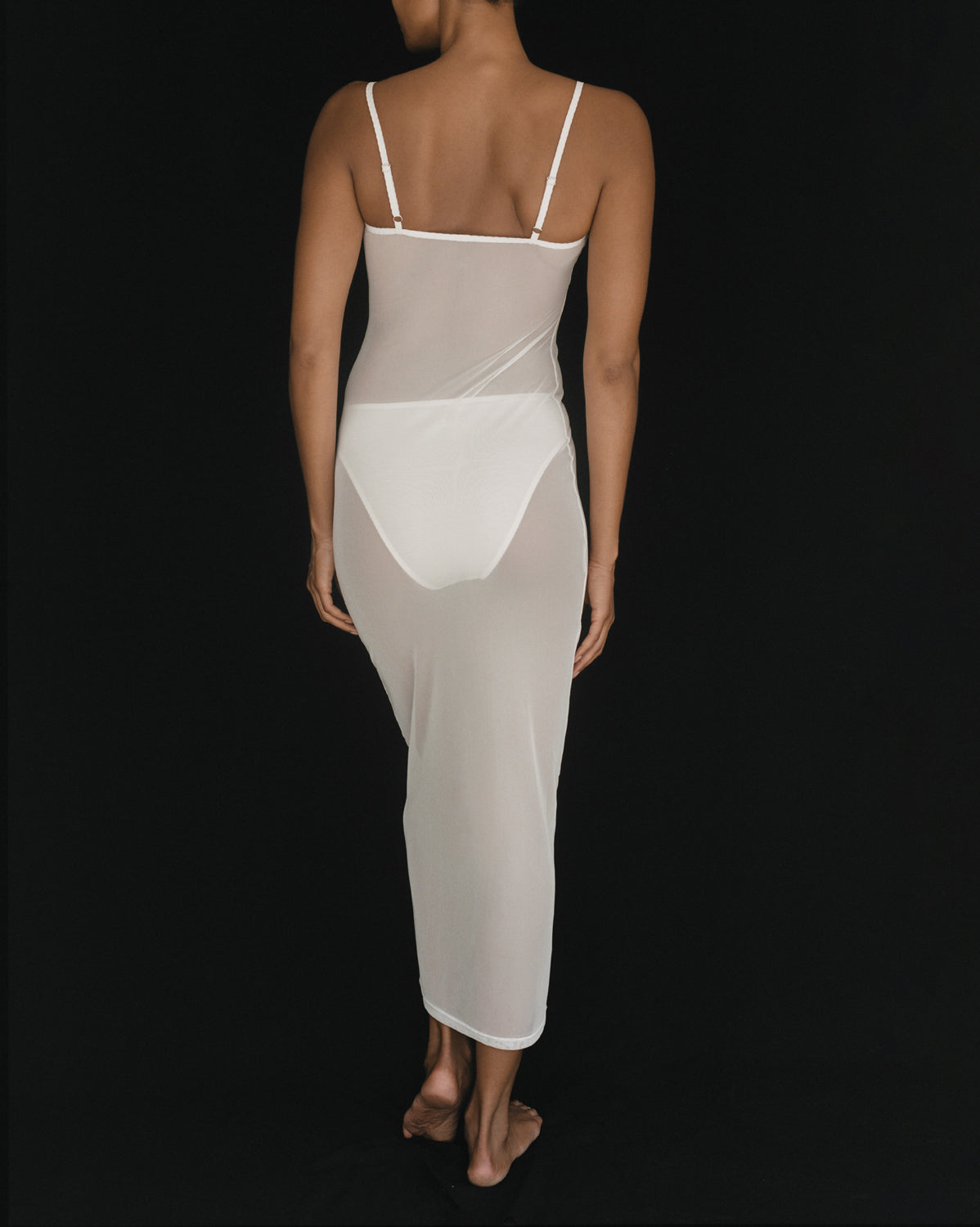 Back view of a model in Kye Intimates Overlay Slip Dress, featuring a sheer white mesh ankle-length slip dress.