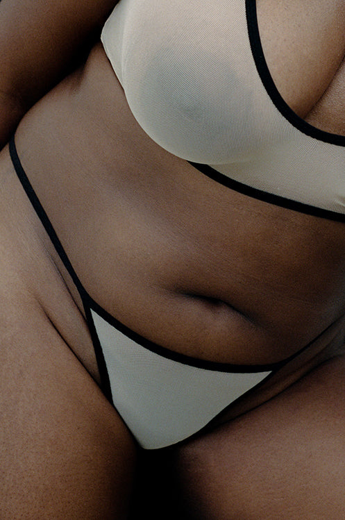 A zoomed in view of the Kye Intimates standard thong in the color black and ecru. Sheer underwear with barely there, minimal coverage. 