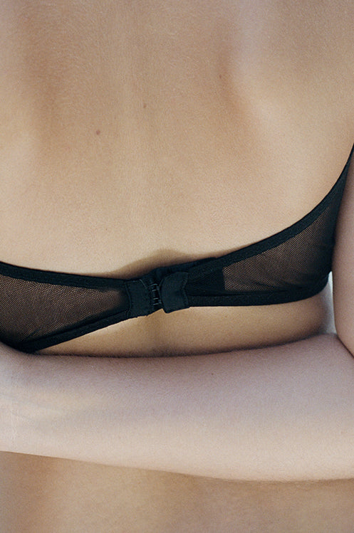 A view of the back of the Kye Intimates Form Bra in the color black. This bra offers the perfect balance between structure and comfort. This sheer bra is wire free, with adjustable shoulder straps and an adjustable back clasp. This wire free v neck bra provides moderate support, and is comfortable yet feminine.