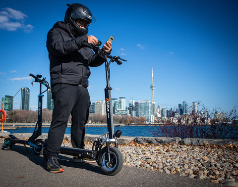 Electric Kickscooter in Toronto, Ontario. Rider wearing a helmet and looking at his phone. CN Tower in the background.