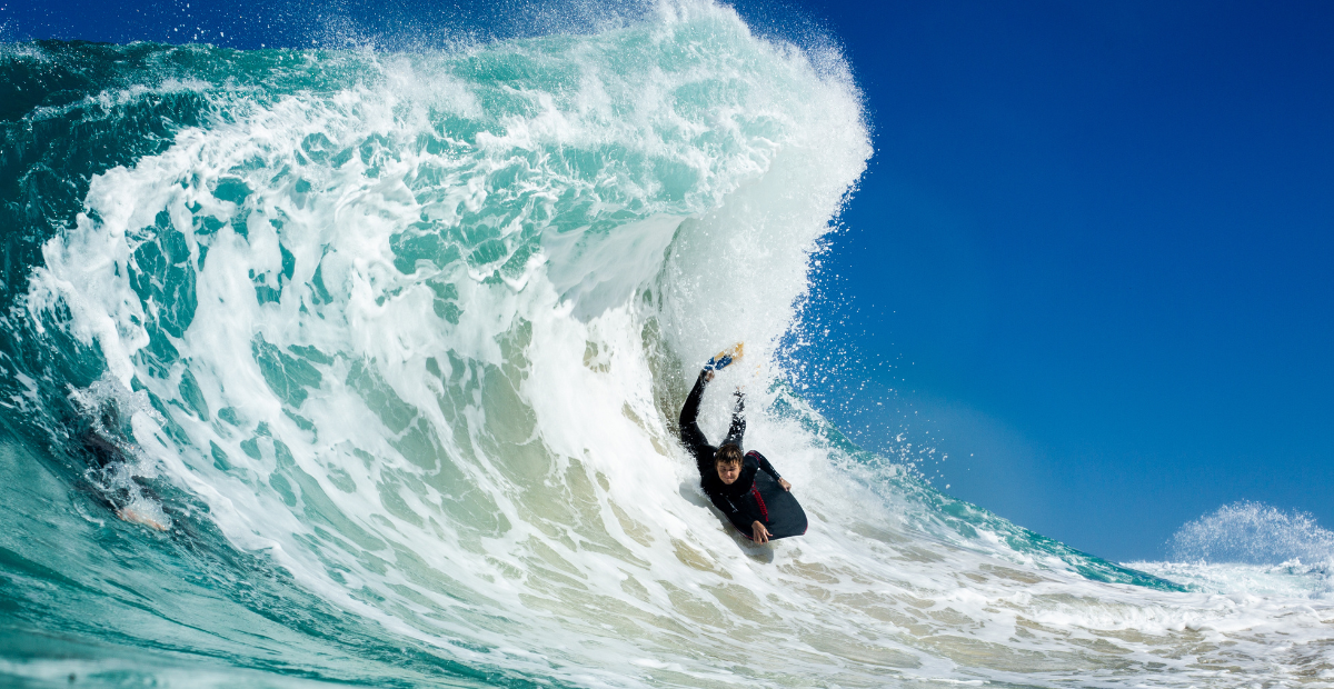A bodyboarder rides in the prone riding style down the face of a massive crashing wave.