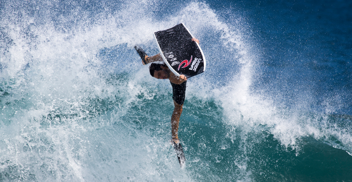 A bodyboarder gets air off a huge wave while holding his board out in front of him.