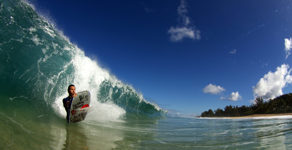 A bodyboarder flexes his board up as he goes down the face of a large crashing wave