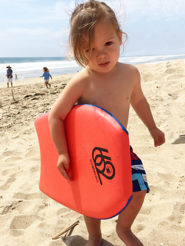 A child holds a bodyboard from 662 bodyboard shop while walking up the beach.