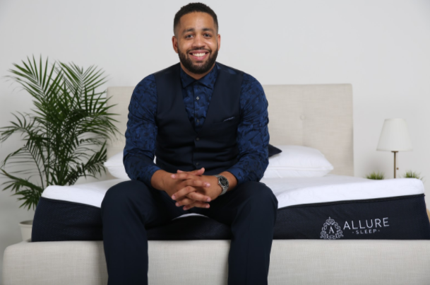 Brand's owner sitting on mattress smiling