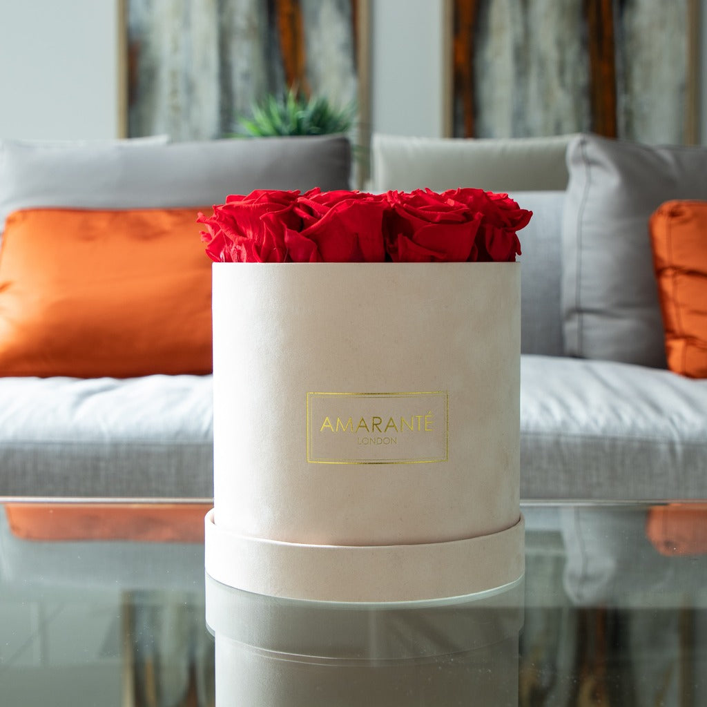 Enchanting anniversary bouquet in red bursting with fiery colours, denoting love, romance, and religious fervour Divine marriage anniversary flowers shown in a blushing beige medium box, on a modern glass table