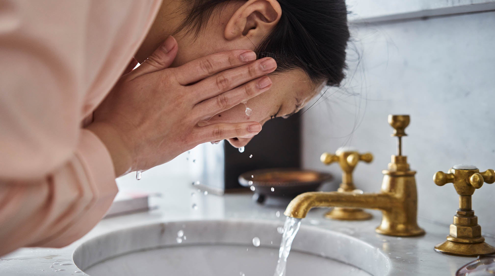 Woman washing her face in front of sink