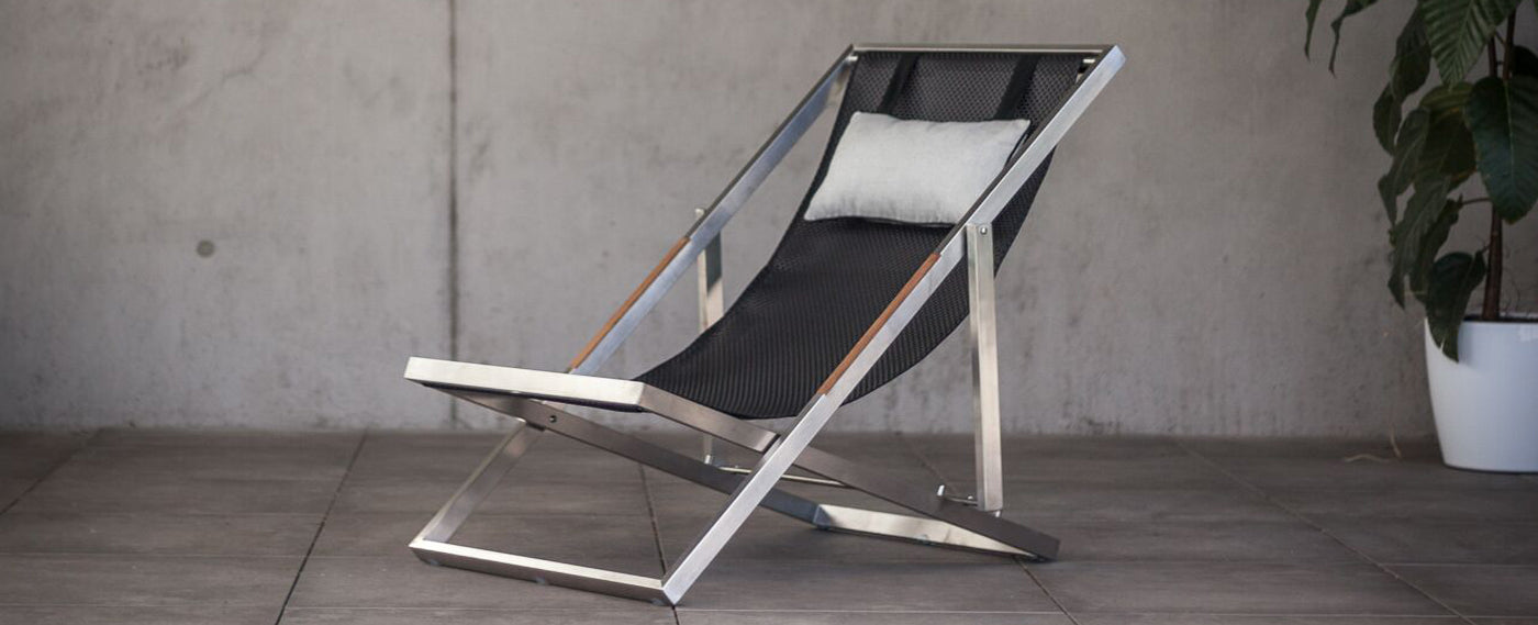 Folding deck chair made of stainless steel elegantly presented in a concrete environment