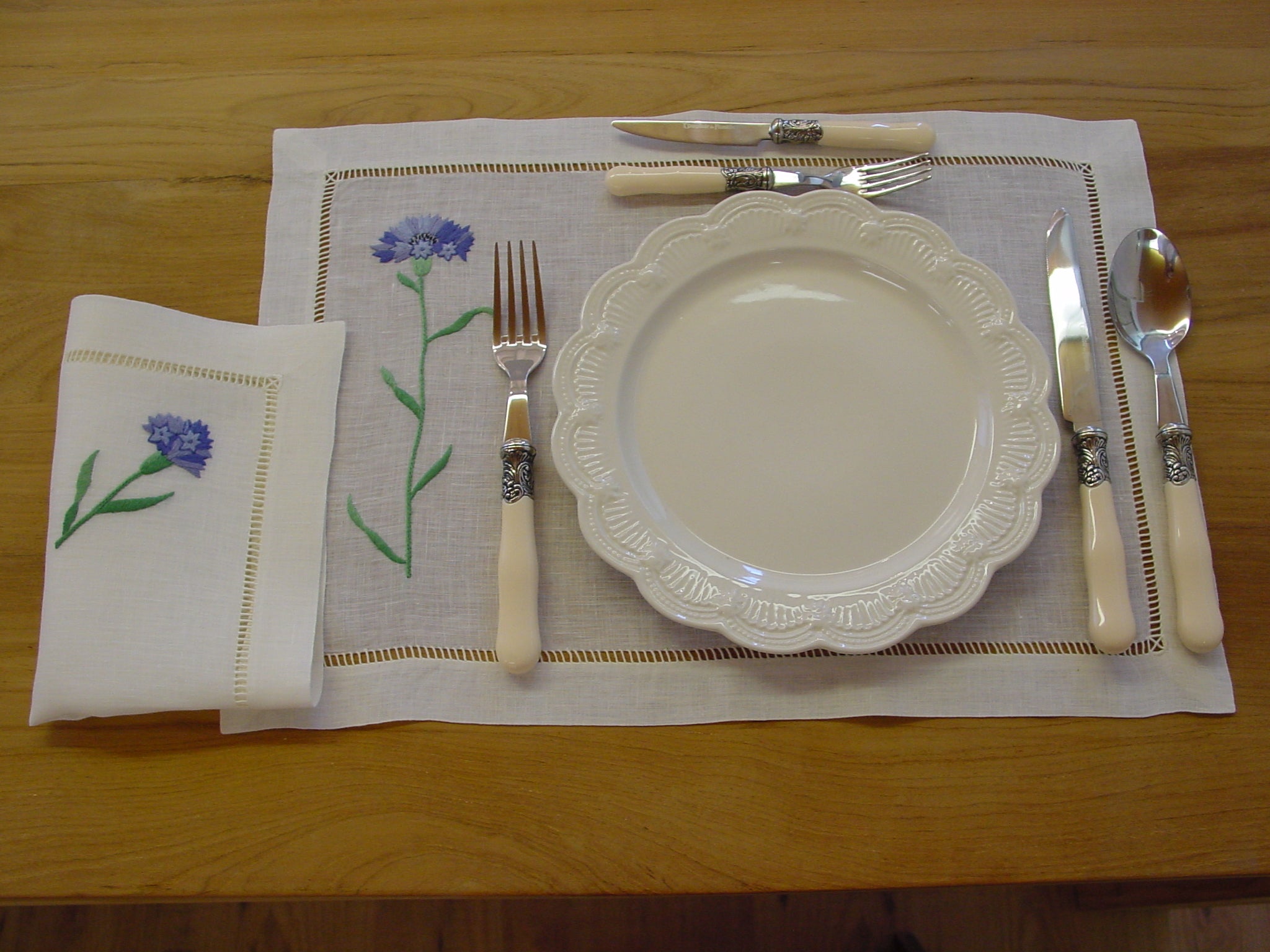 Serviette en lin brodée de bleuets sur table décorée de couverts, assiettes et set de table