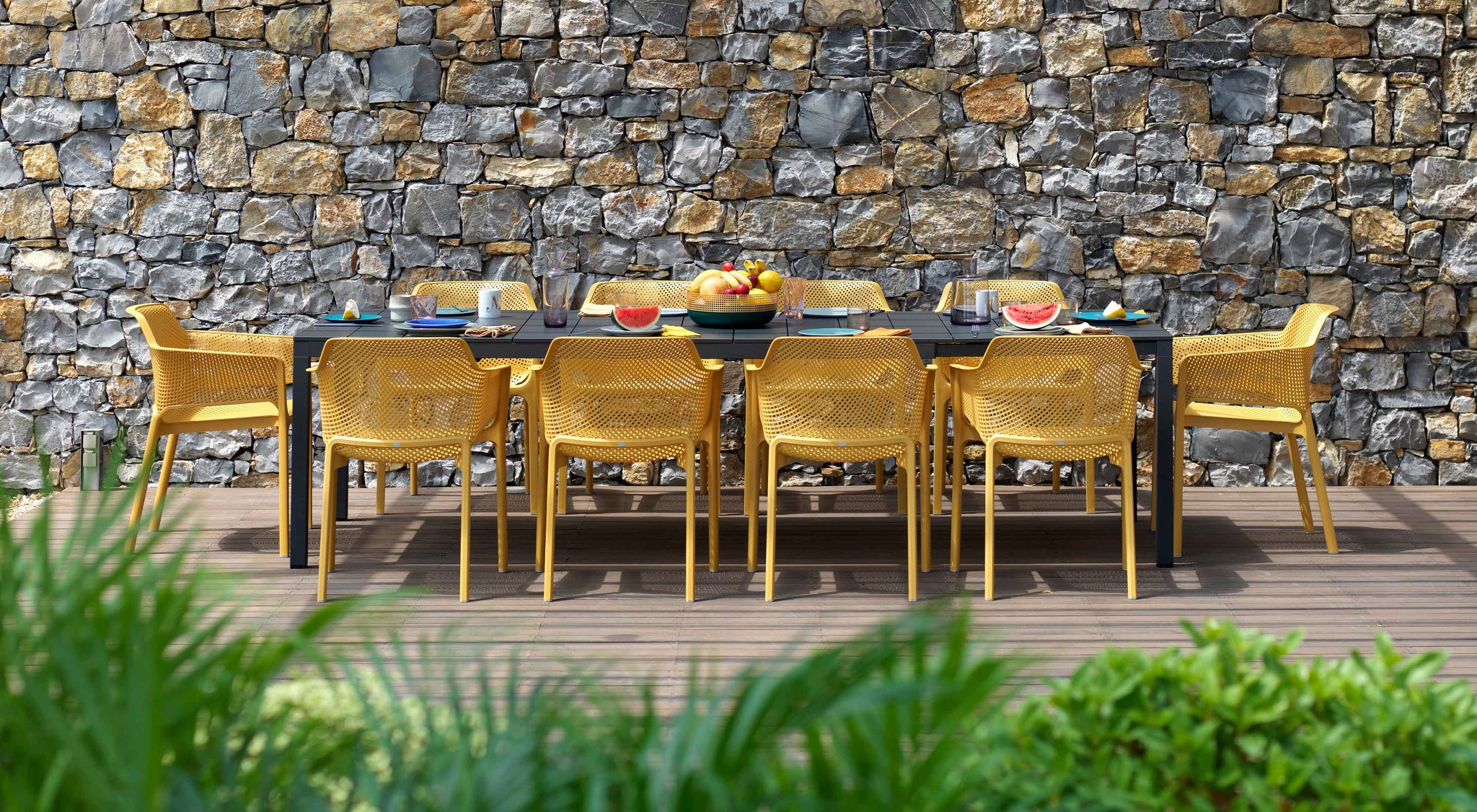 Nardi Net seating group with 10 chairs in the color Senap in front of a natural stone wall