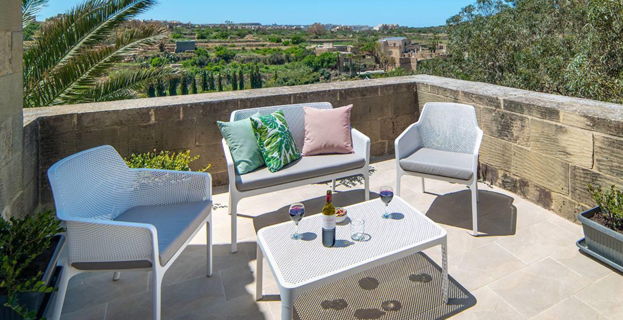 Table en filet, avec chaises en filet et banc en filet blanc sur terrasse avec vue sur un village méditerranéen