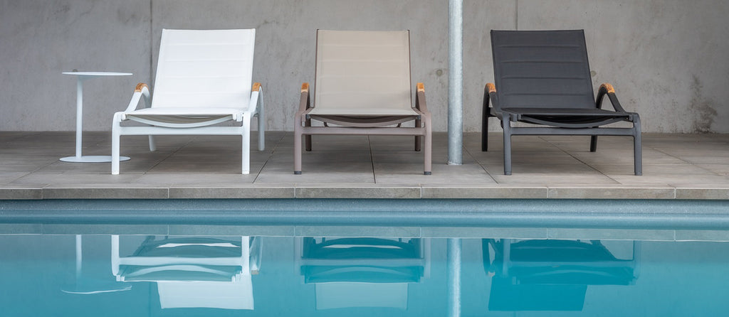 Vitoria sun lounger in three colors presented in a very modern way by the pool in front of a concrete wall