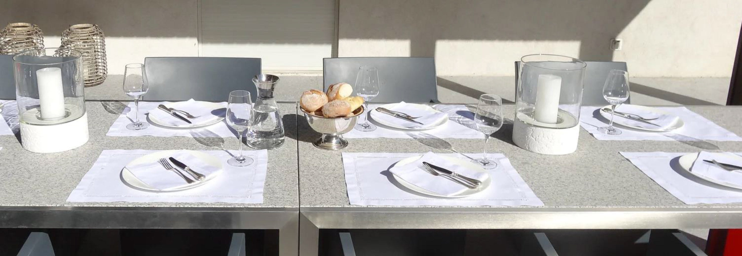 Stoffservietten auf Gartentisch mit Kerzen im großen Windlicht und Tellern mit Besteck undf Tischsets dekoriert