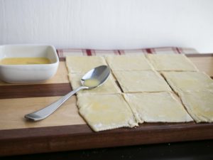 Unroll 1 sheet of puff pastry, and cut into 9 squares. Use a spoon to brush egg wash on each square. The egg wash is helps the pastry stick together. 