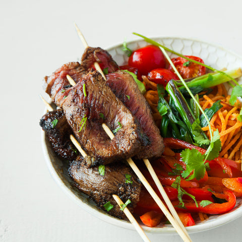 Jamaican Jerk Skewers on top of a bowl of sliced peppers and tomatoes.