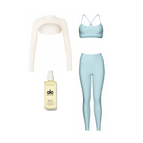 An image of product flatlays including Alo’s Head-To-Toe Glow Oil, a pair of light blue high-waisted leggings, a matching sports bra, and an ivory long sleeve ultra-cropped shrug. 