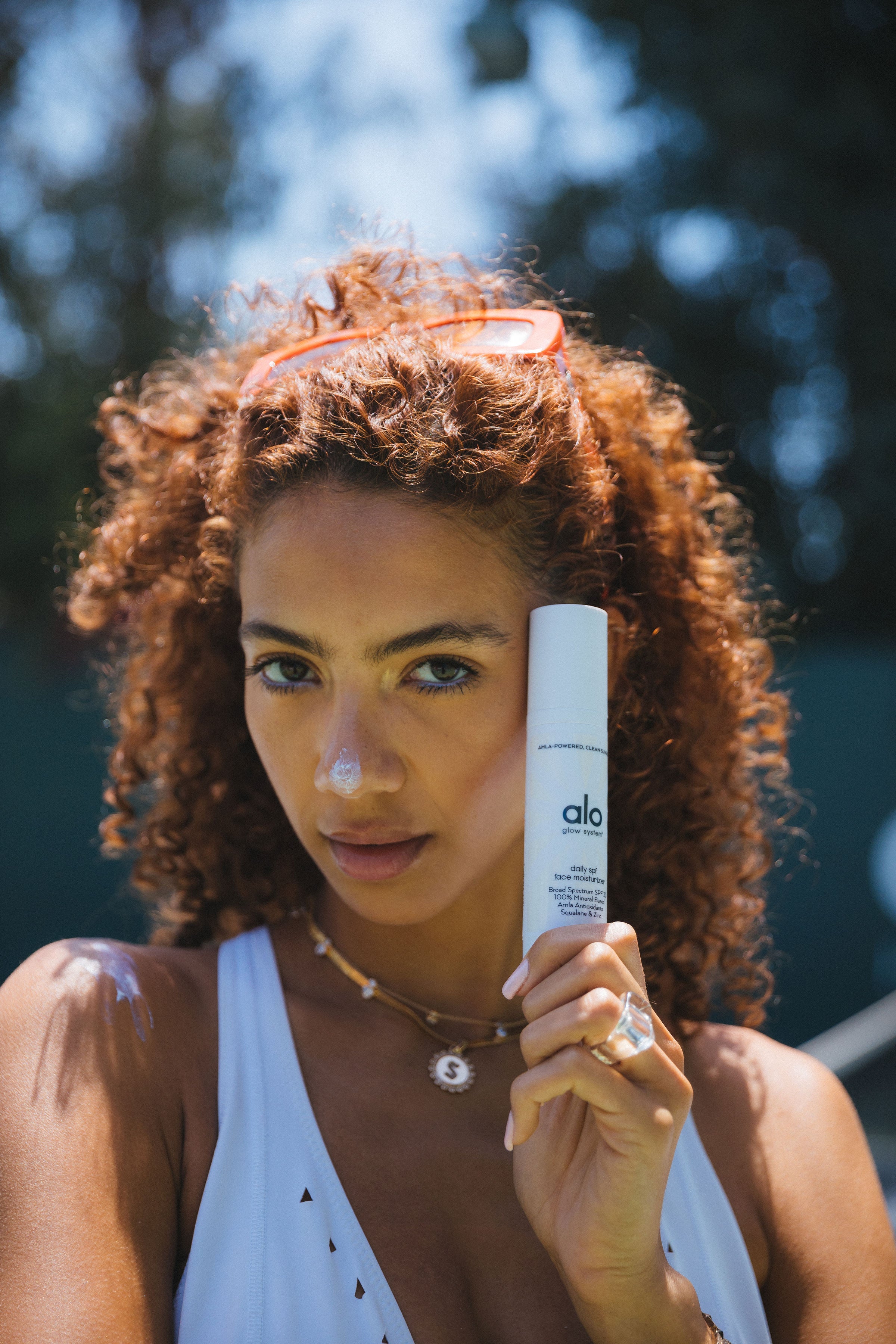 Woman with curly red hair poses with Daily Moisturizing SPF bottle in her hand and white cream dotted on her nose. 