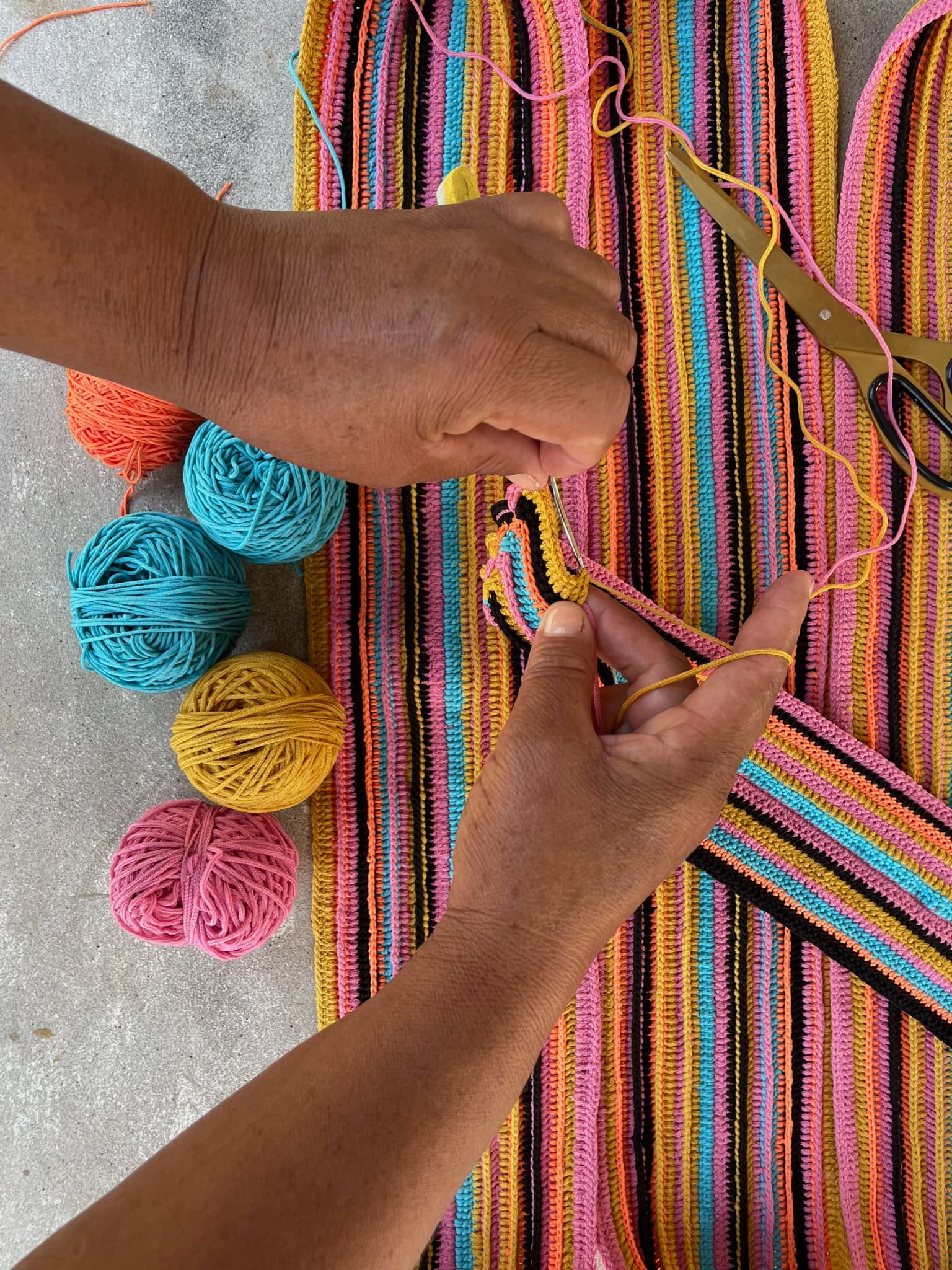A  close-up image of two hands weaving a long strip of colorful textile.  