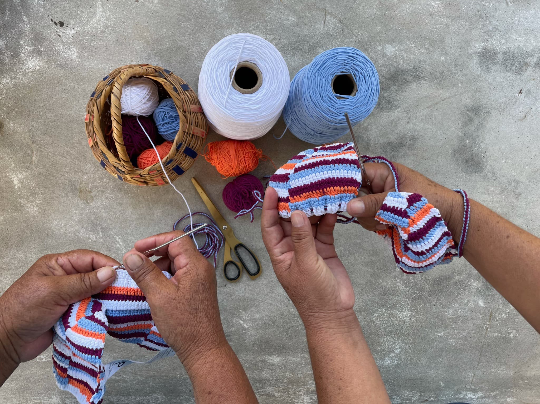 A close-up image of two sets of hands each weaving a Praia Bikini Top in a pattern of vibrant horizontal stripes.  