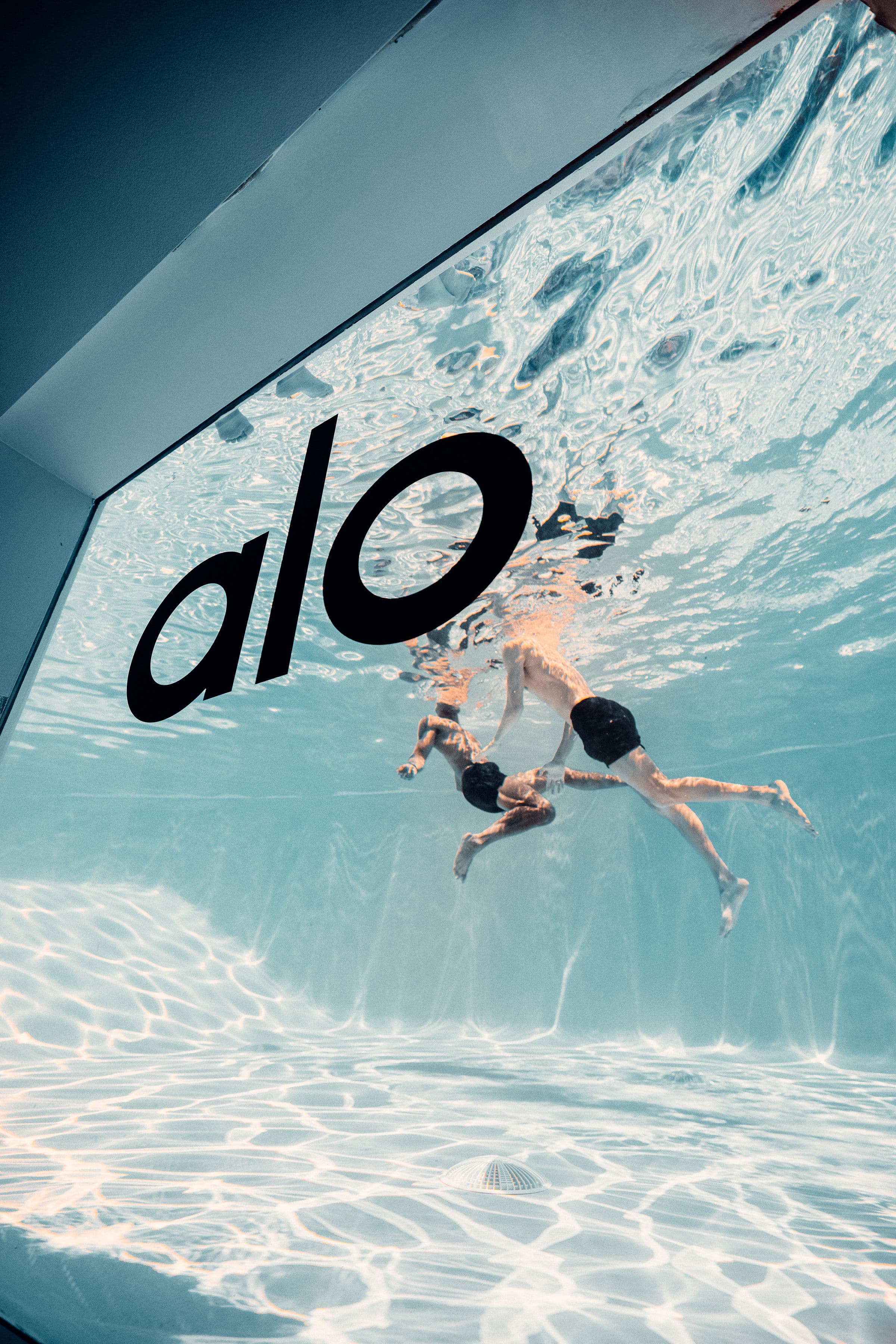 An underwater photo of two men swimming in the pool at Alo Summer House taken from an underground window that looks directly into the pool.  