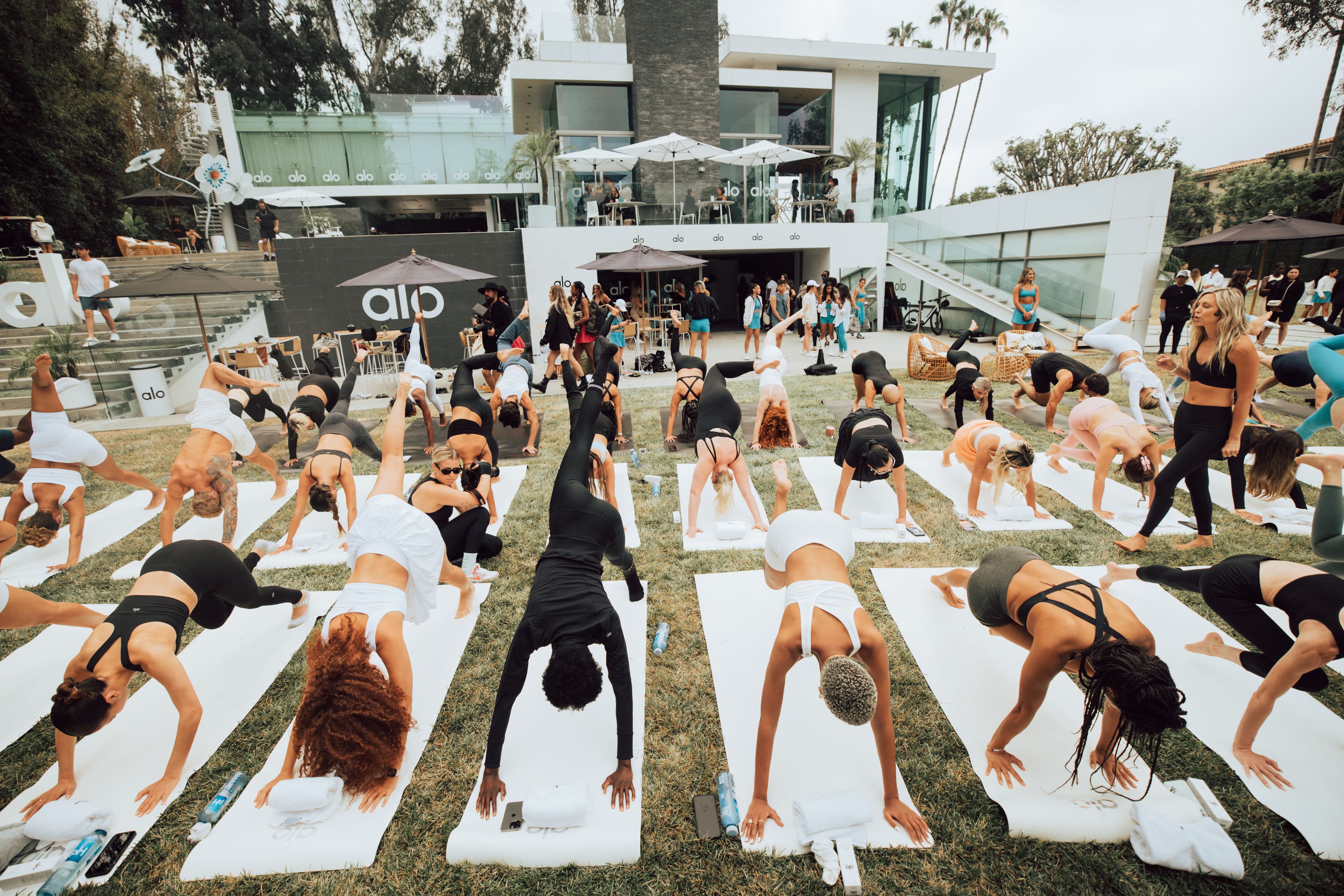 A photo of the yoga flow at Alo Summer House 2022 that took place on the lawn with a background view of the house and pool. 