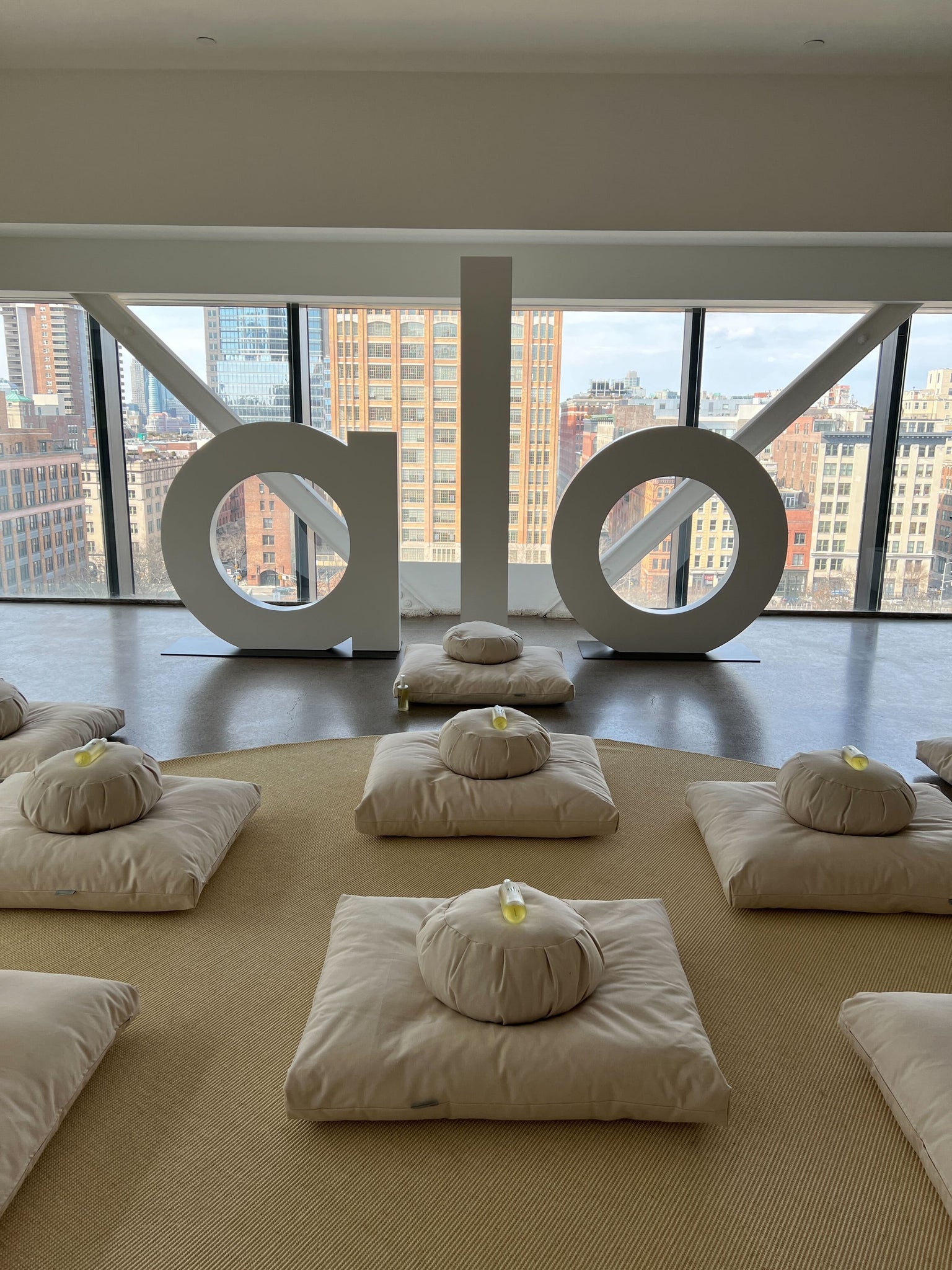 A photo of the meditation space during NYFW at Alo’s pop-up at Spring Studios displaying meditation pillows topped with a bottle of Alo’s Magnesium Reset Spray. 