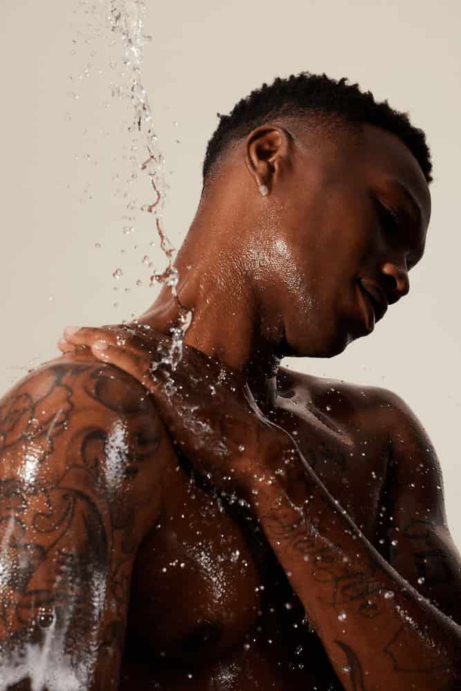 Alo Wellness shot of tattooed man in shower with water splashing over him. 