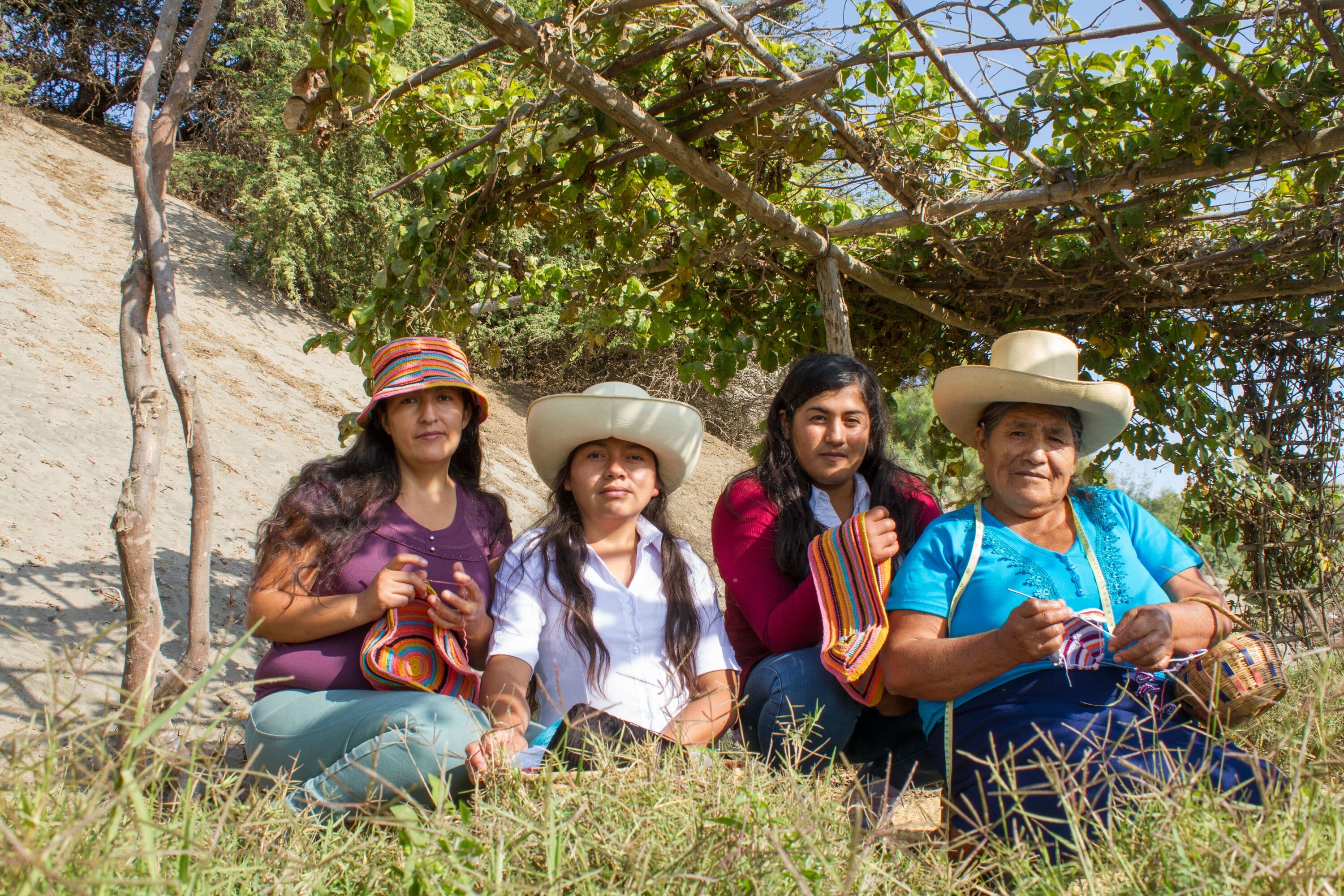 Four women posing for a photo underneath a pergola covered in vines while weaving using the Andean Tramado Crochet technique.  