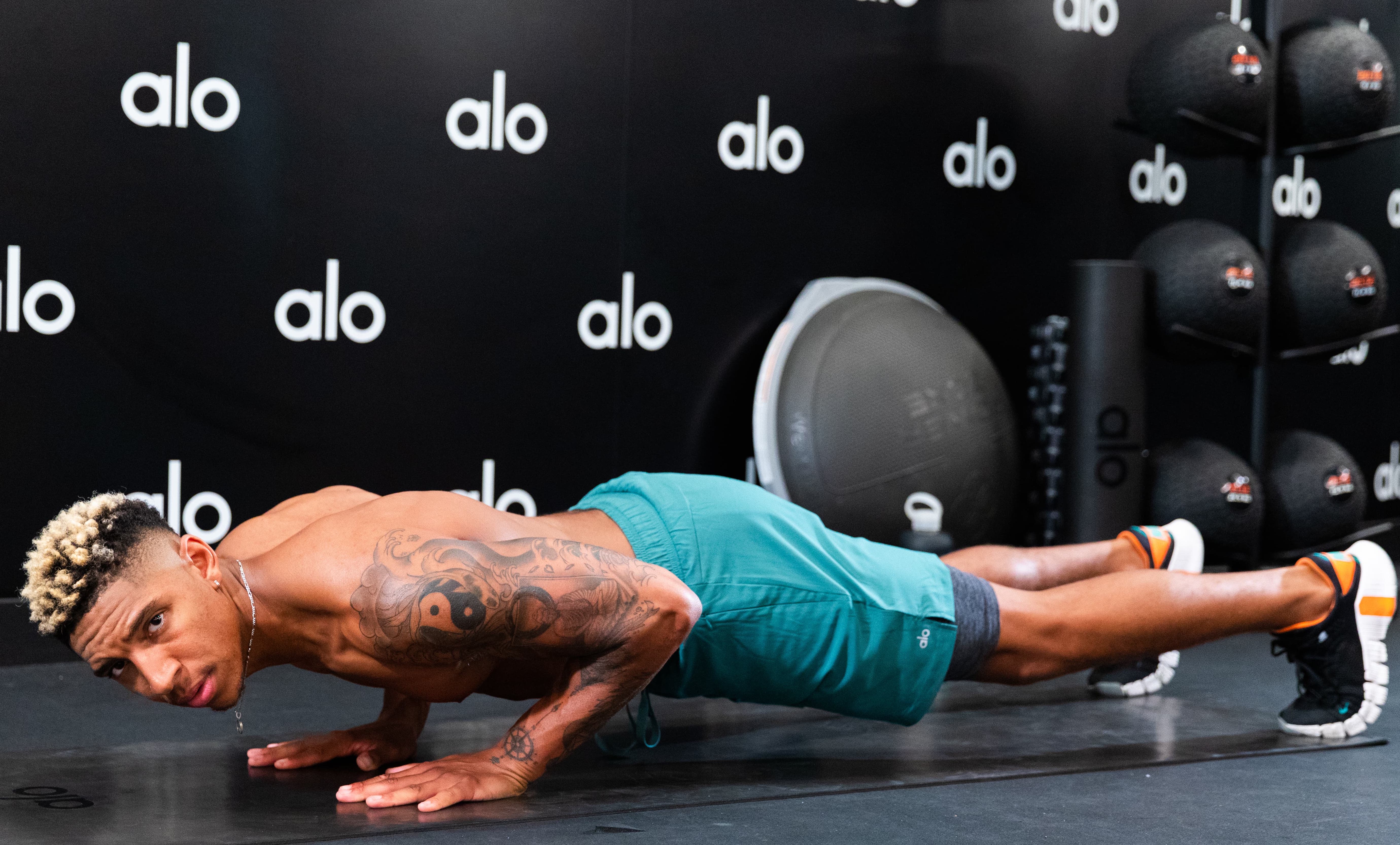 Louis Chandler in a pushup position while wearing a pair of men's teal activewear shorts within Alo's Wellness Club filming for his newest classes on Alo Moves.