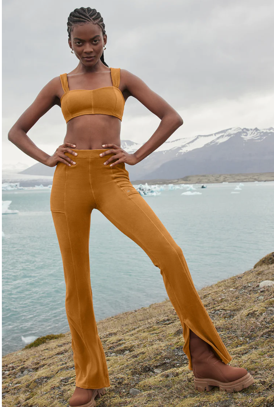 Alo model wearing the Micro Corduroy Winter Break Flares and matching bra while standing on a cliff overlooking the ocean in Iceland with mountains and icebergs in the background. 