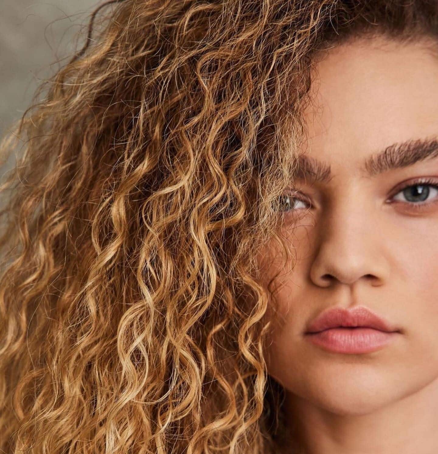 Close up of model with healthy, blonde curly hair and full brows 