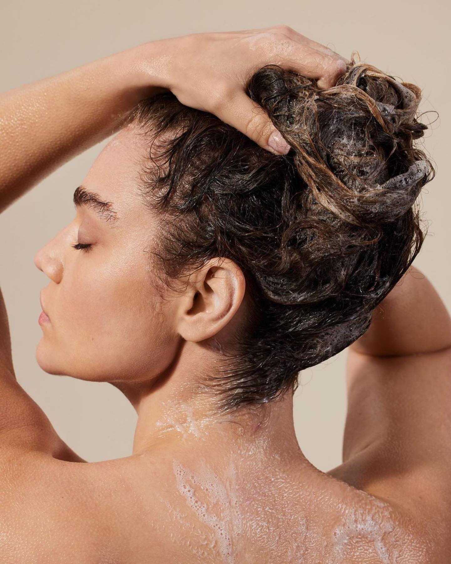 Back shot of woman with dark hair massaging her wet hair and scalp. 