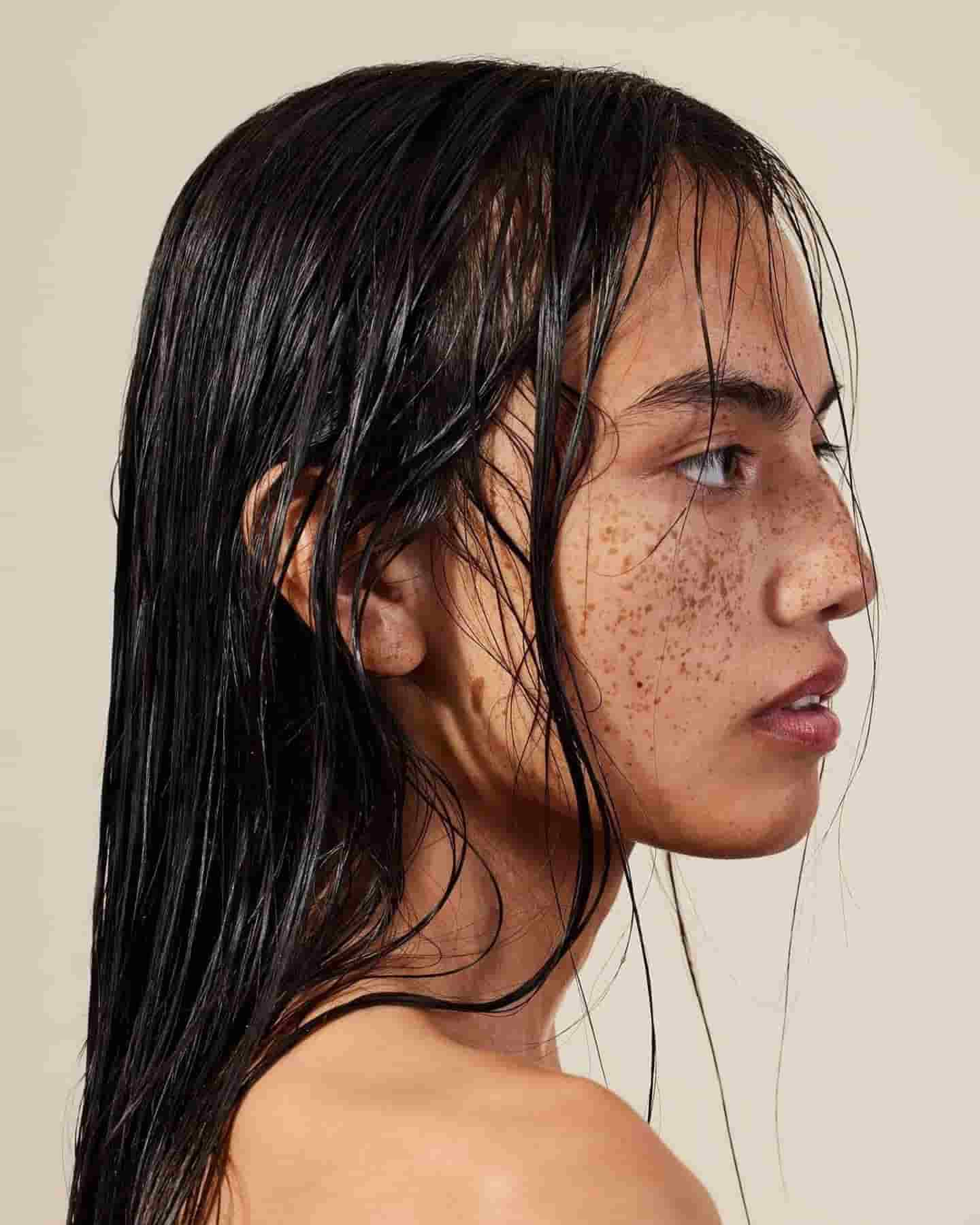 Close side profile, beauty shot of dark-haired model with freckles and wet hair. 