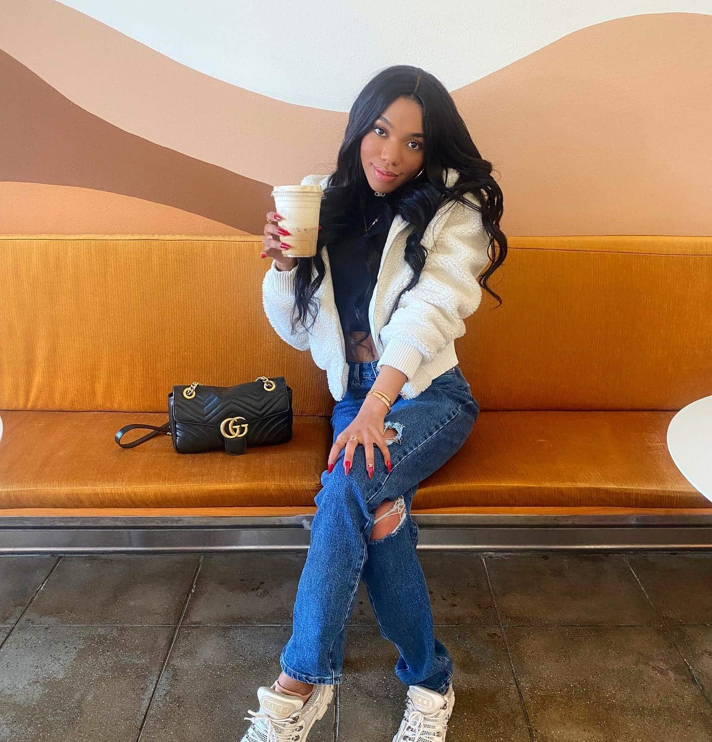 Teala Dunn porte une veste Sherpa Foxy ivoire tout en dégustant un café dans un café.